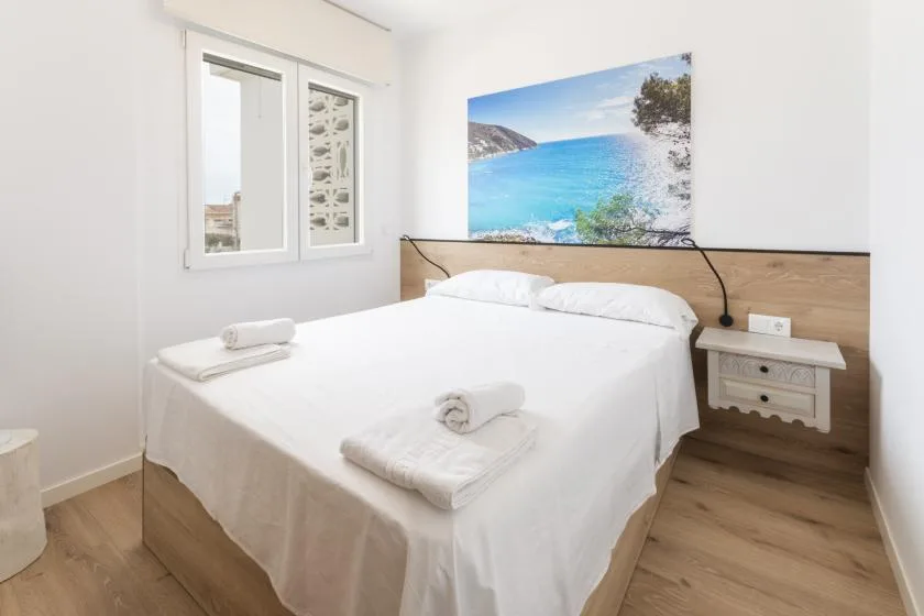 Un dormitorio luminoso con una cama bien tendida y una imagen costera sobre el cabecero.