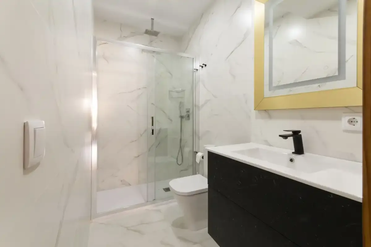 Un baño luminoso con ducha de vidrio y un mueble oscuro.