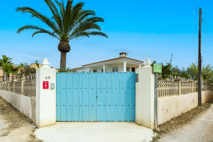 Una puerta azul y un muro bajo están frente a una casa bajo una palmera.