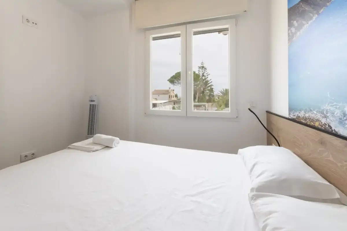 Un dormitorio con una cama bien tendida bajo una ventana.