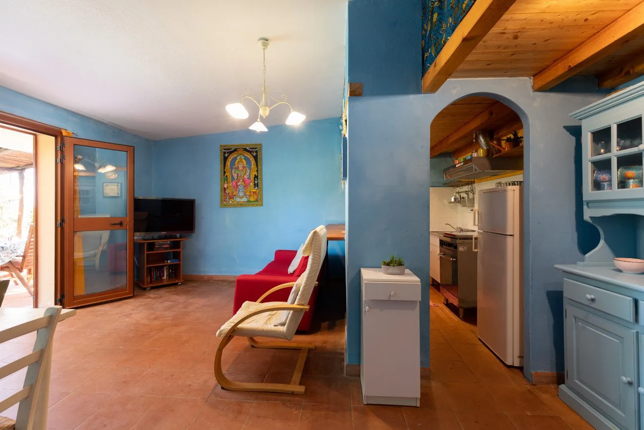 Una sala con paredes azules se abre a una cocina, con asientos y un televisor.