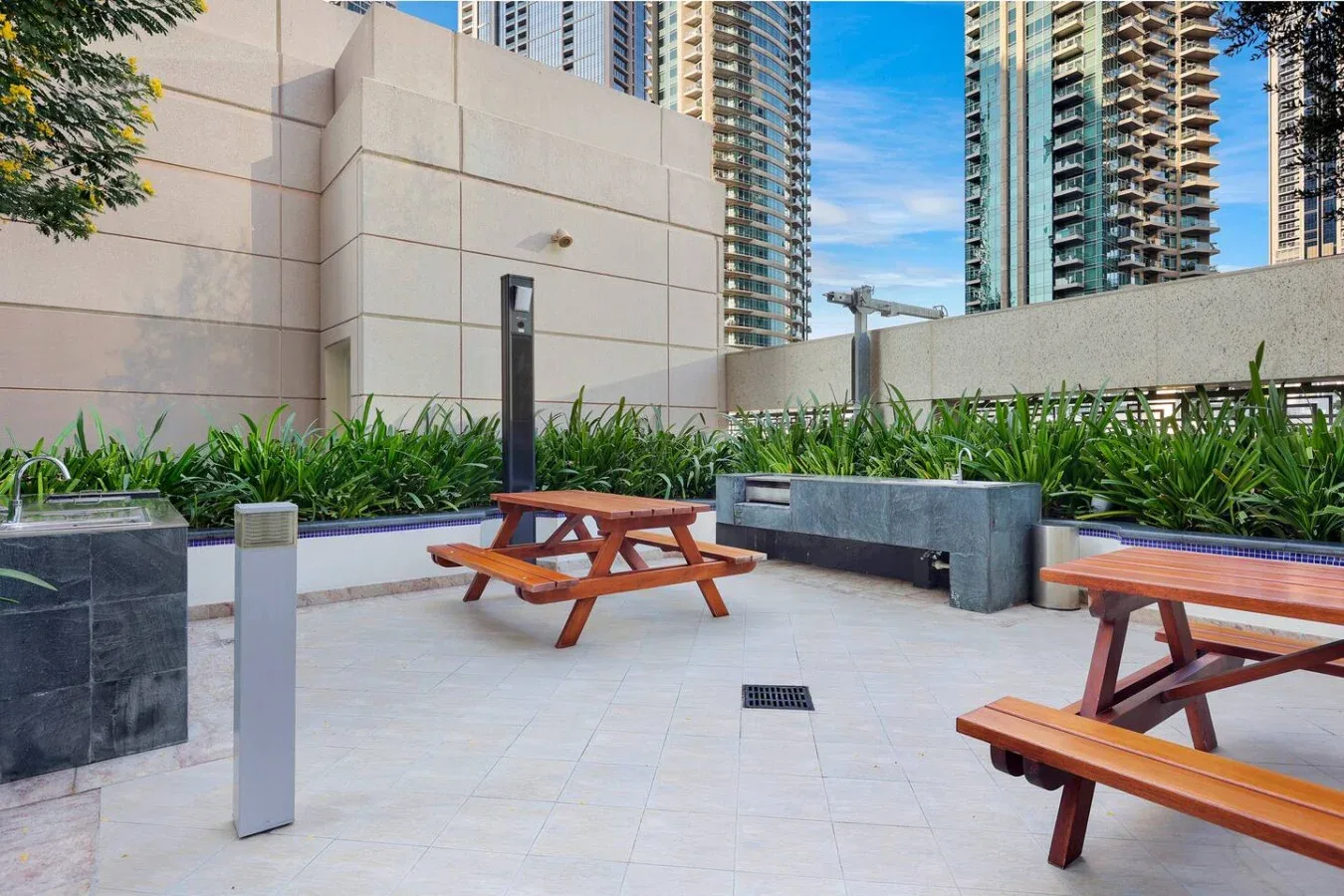 Una zona exterior pavimentada tiene mesas de picnic de madera y jardineras elevadas.