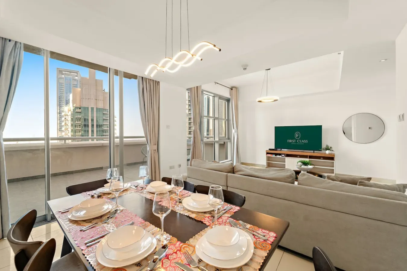 Una luminosa zona de comedor y sala tiene una mesa puesta junto a grandes ventanales.