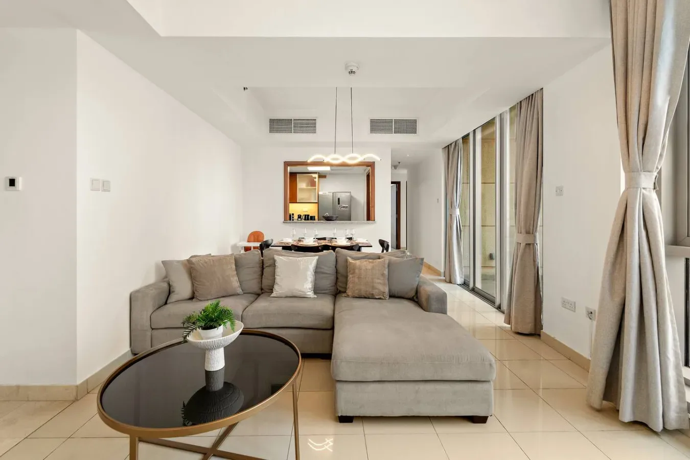 Una sala luminosa con un área de asientos seccionales y grandes ventanas con cortinas.