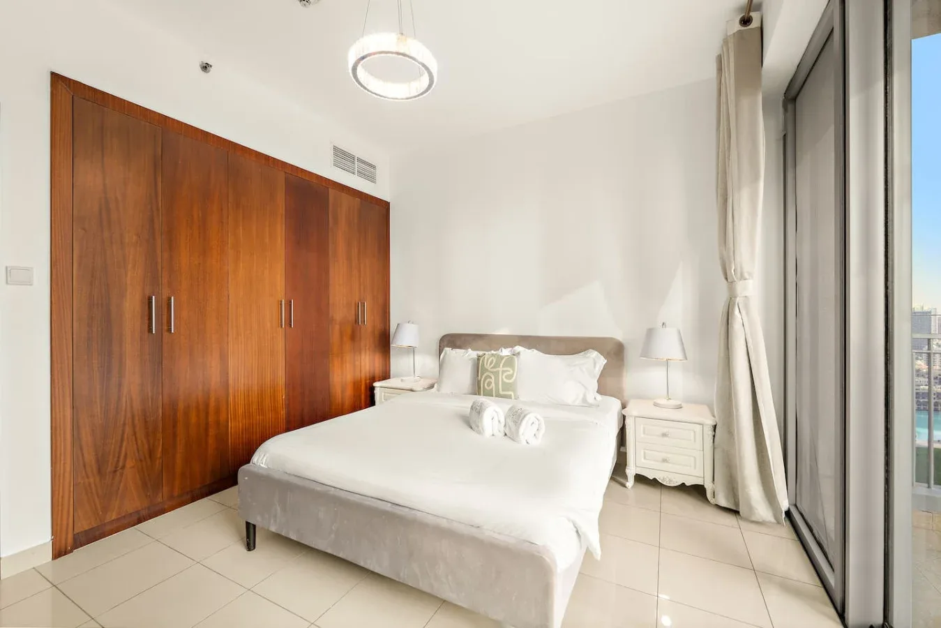 Un dormitorio luminoso con una cama, mesitas de noche y un gran armario de madera.