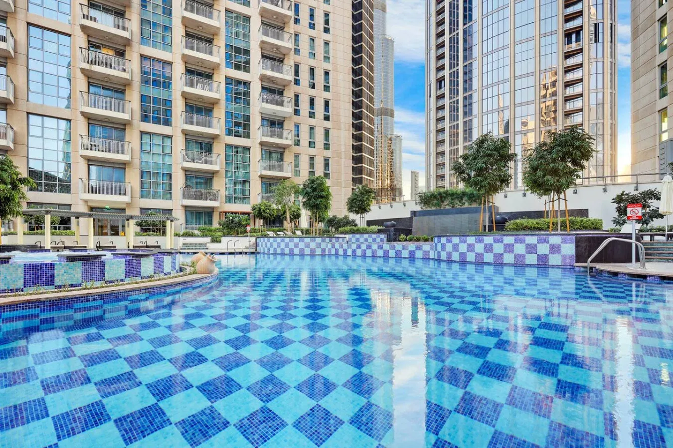 Una piscina al aire libre con azulejos azules estampados está entre edificios altos.
