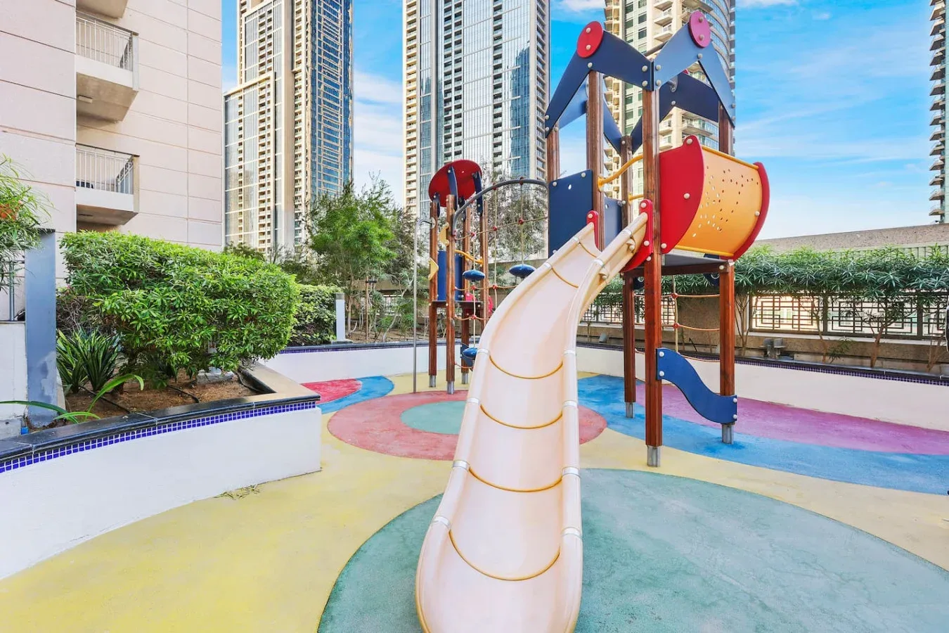 Un colorido parque infantil al aire libre con toboganes y estructuras para trepar entre edificios altos.