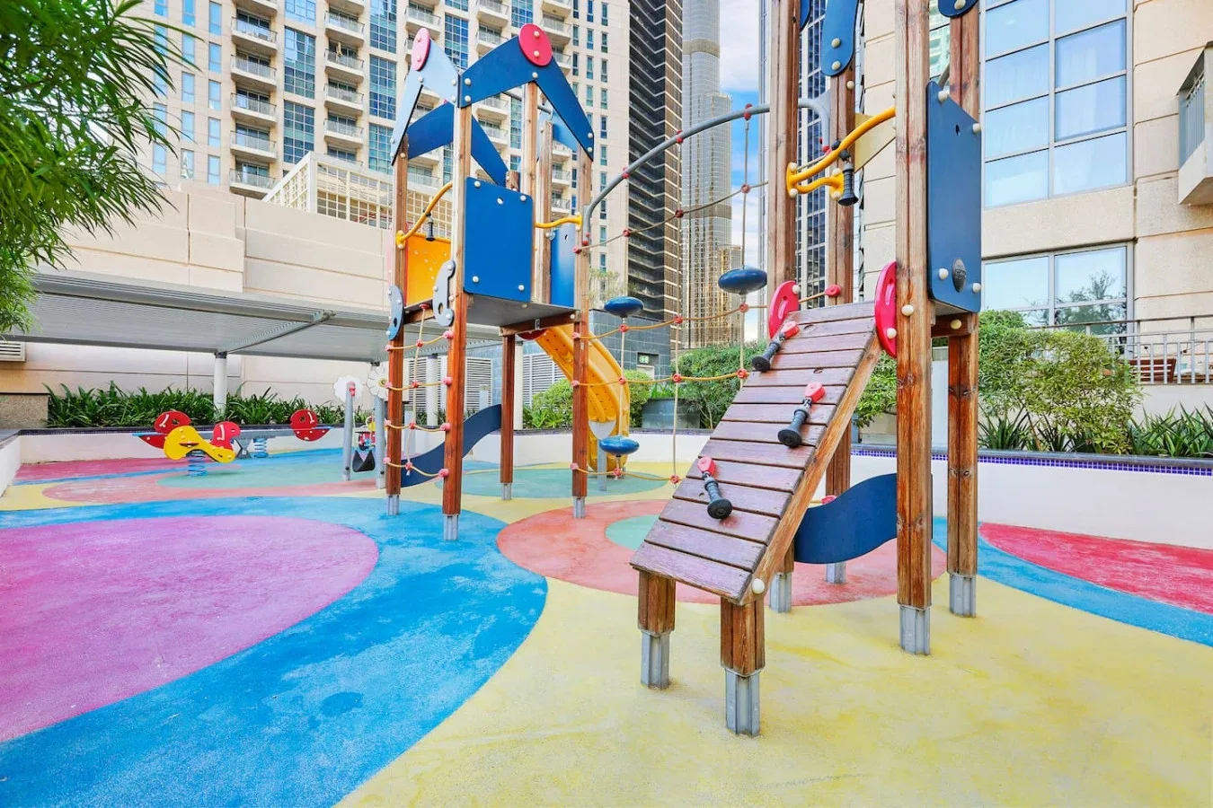Un parque infantil al aire libre tiene estructuras para trepar y toboganes sobre un suelo de colores.