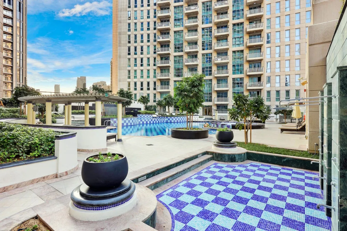 Un patio con piscina al aire libre, azulejos azules a cuadros y edificios altos alrededor.
