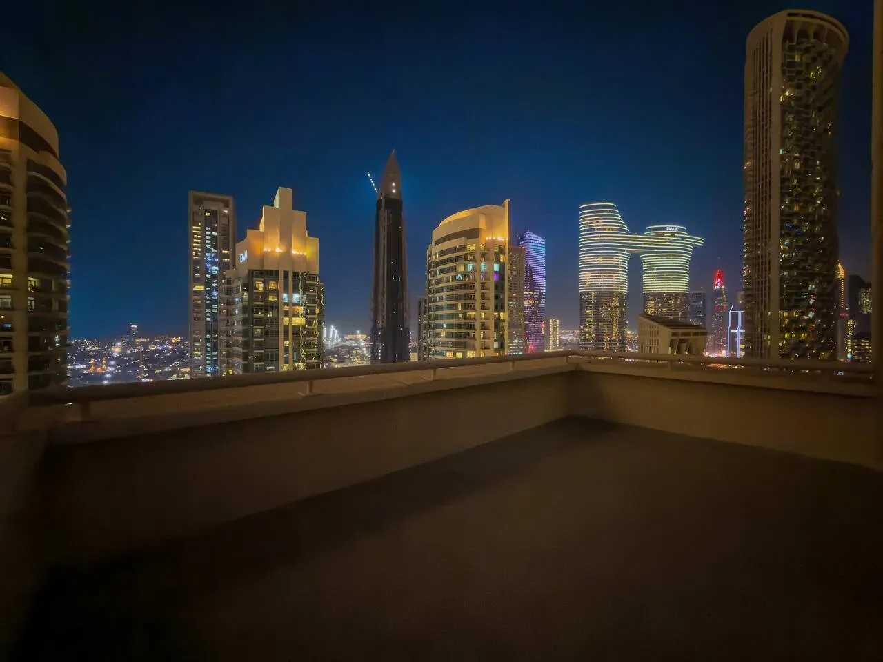 Una terraza en la azotea ofrece vistas de un horizonte urbano iluminado por la noche.
