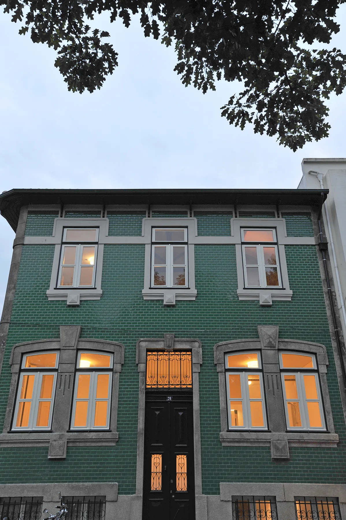 A green-tiled building facade with illuminated windows and a central entrance.