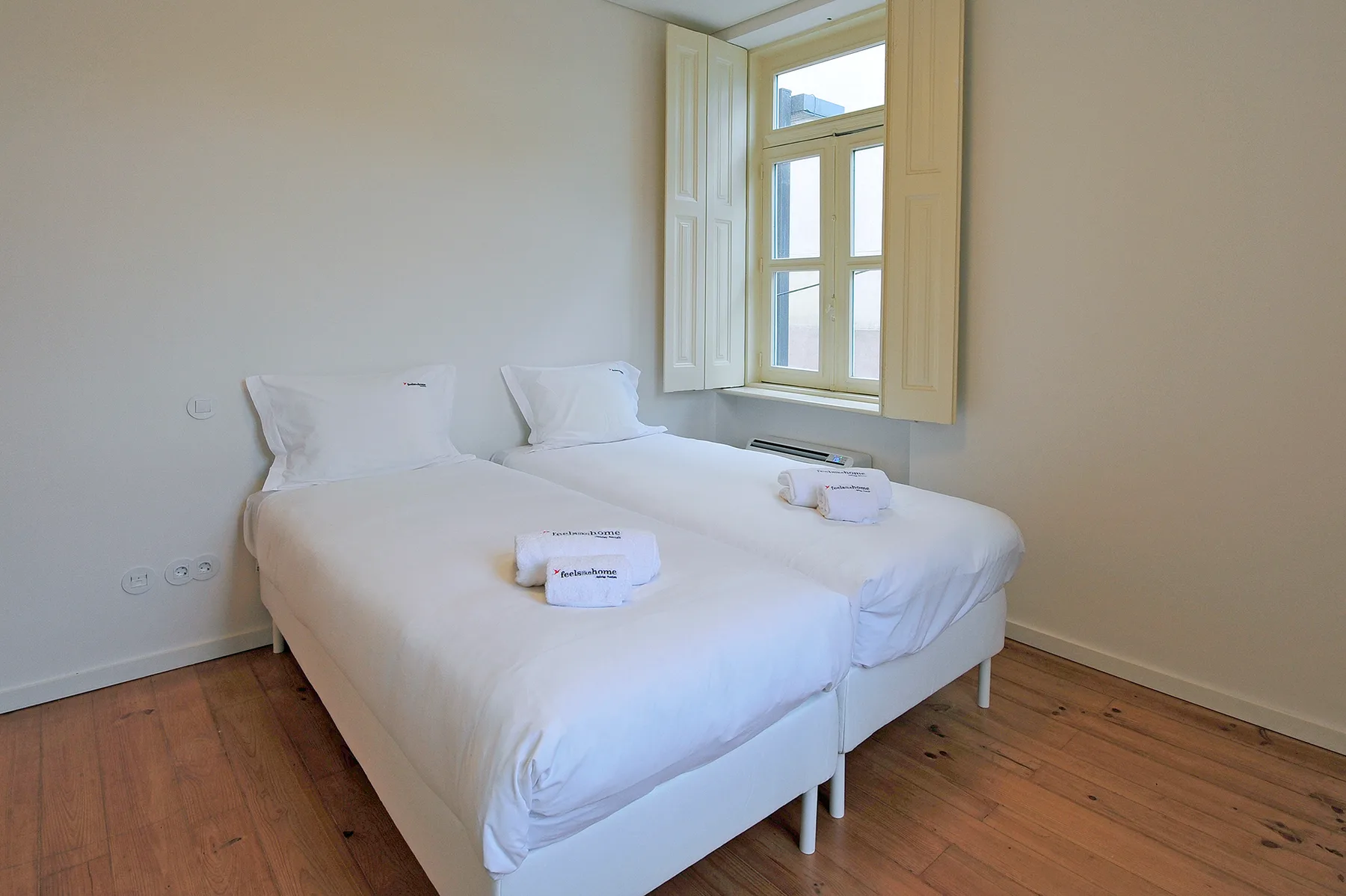 A bright bedroom with a white bed beside a large window.