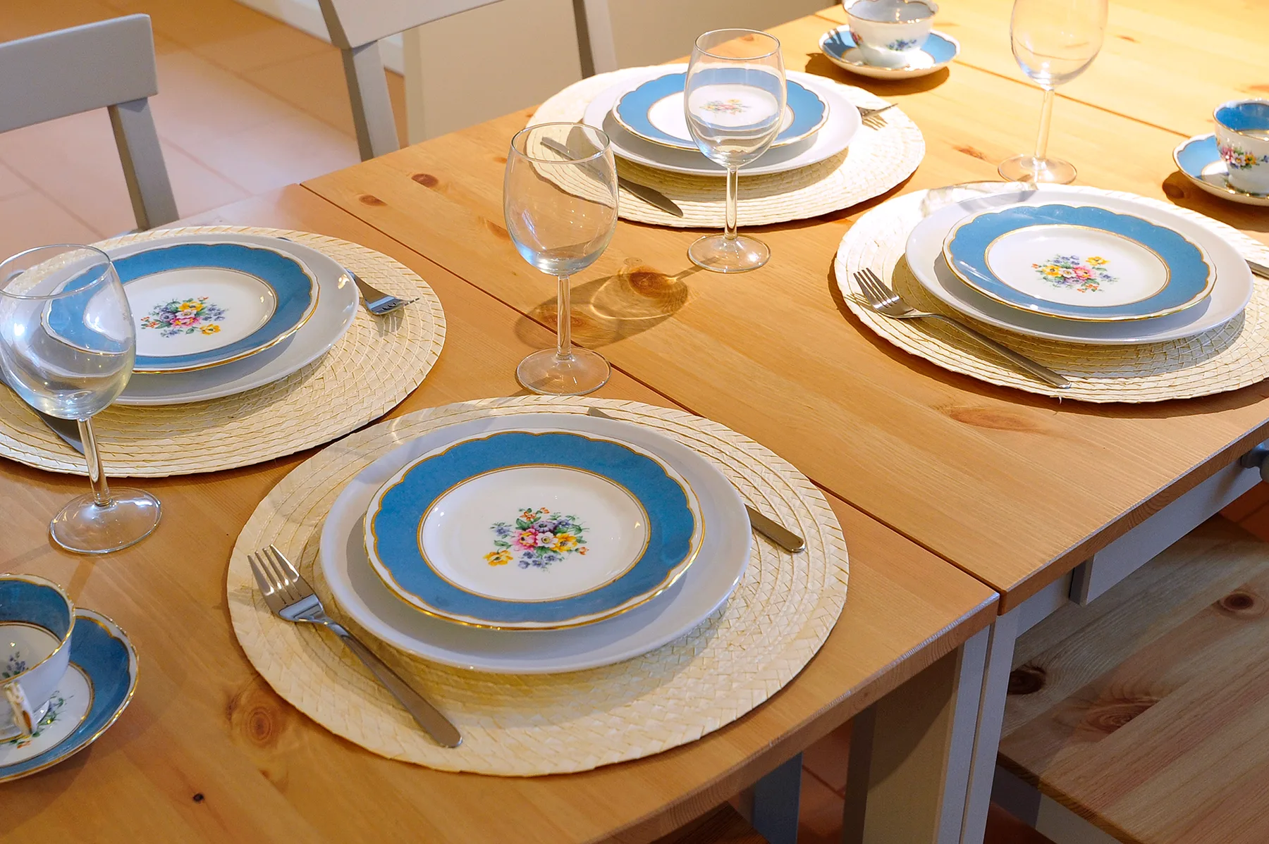 A dining table is set with patterned plates, woven placemats, and glassware.