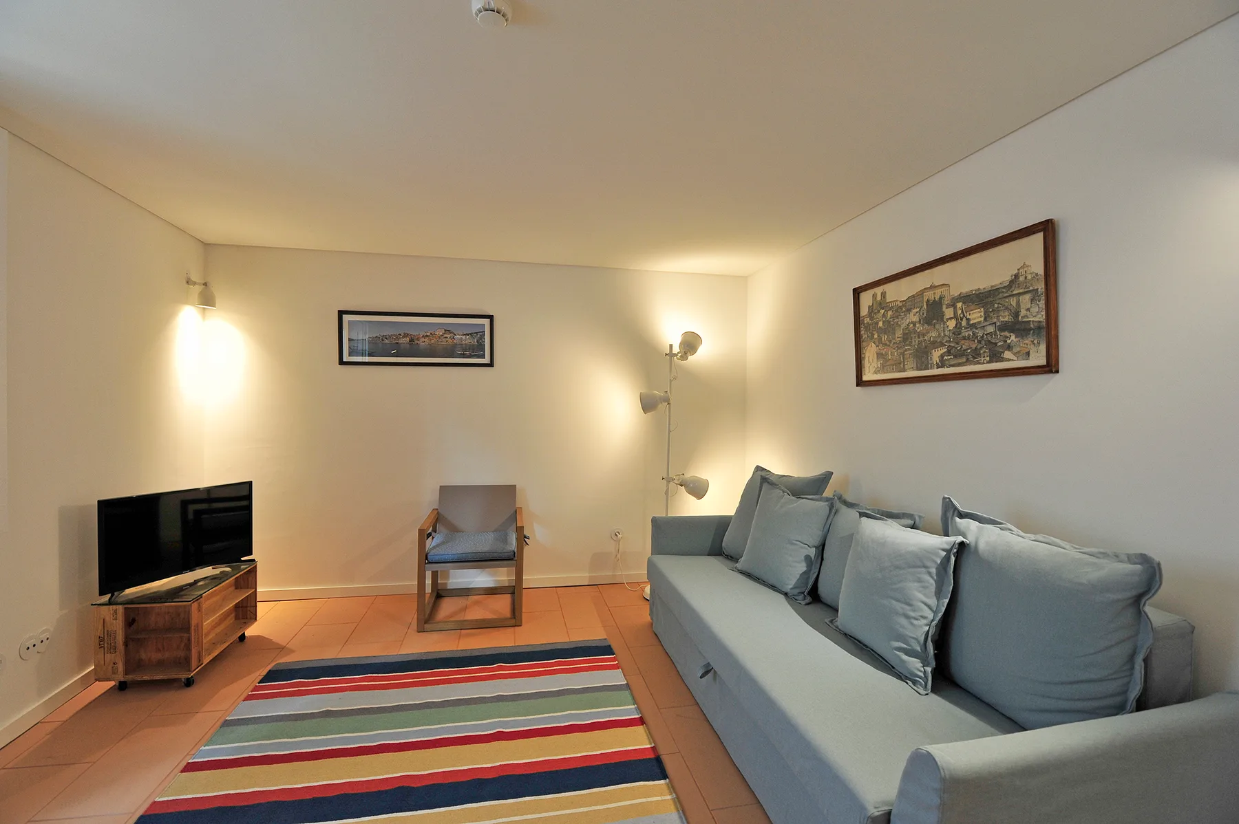 A living room with a sofa, television, and colorful striped rug.