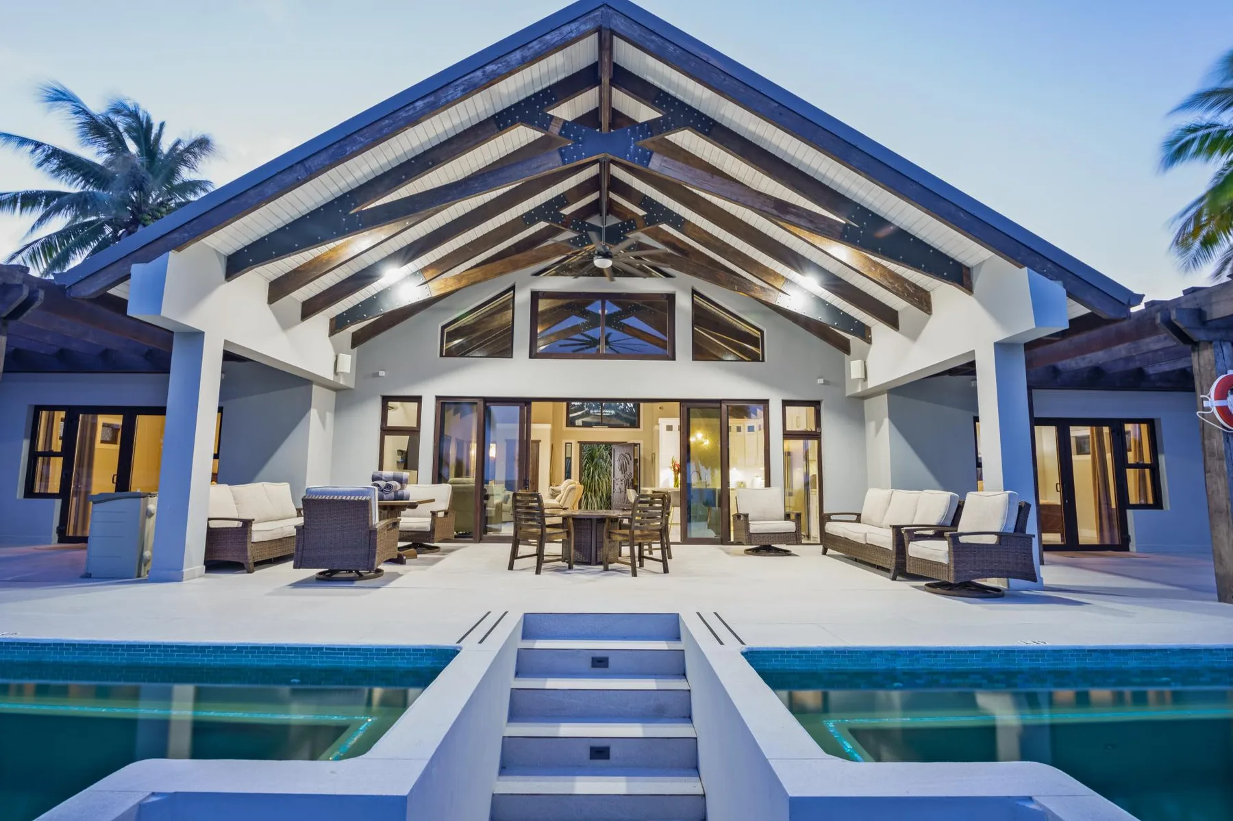 A covered outdoor seating area faces a pool beneath an open timber roof.
