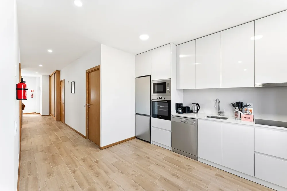 A bright kitchen with white cabinets and a hallway alongside.