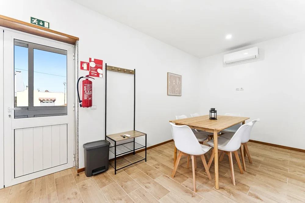 A dining area with a wooden table and white seating beside a glass door.