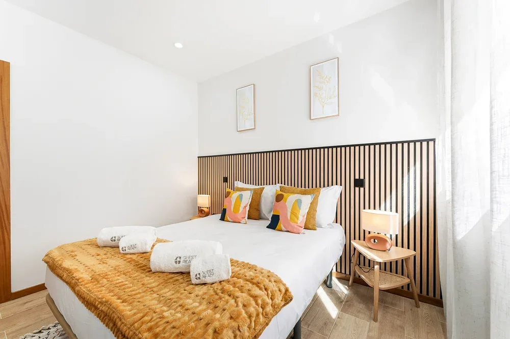 A bright bedroom features a bed with colorful pillows and a woven blanket.