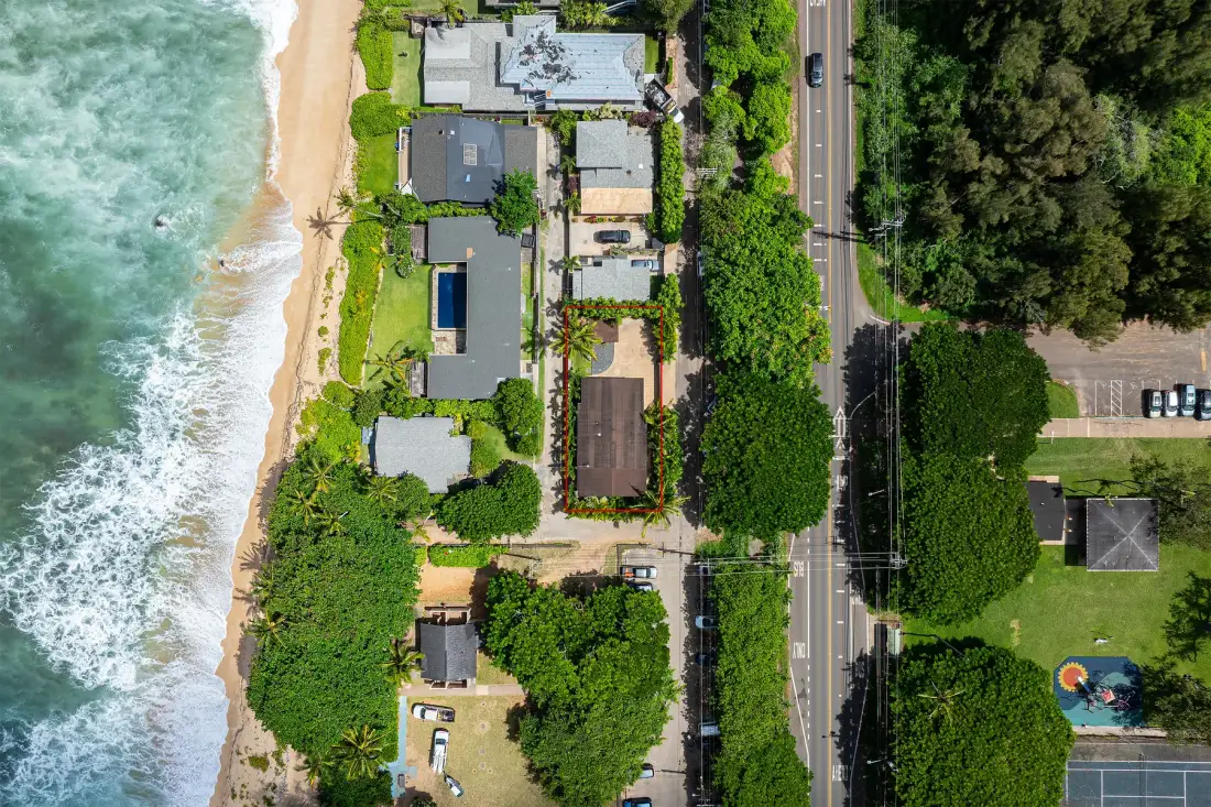 Una vista aérea muestra una propiedad costera junto a una playa de arena y una carretera arbolada.