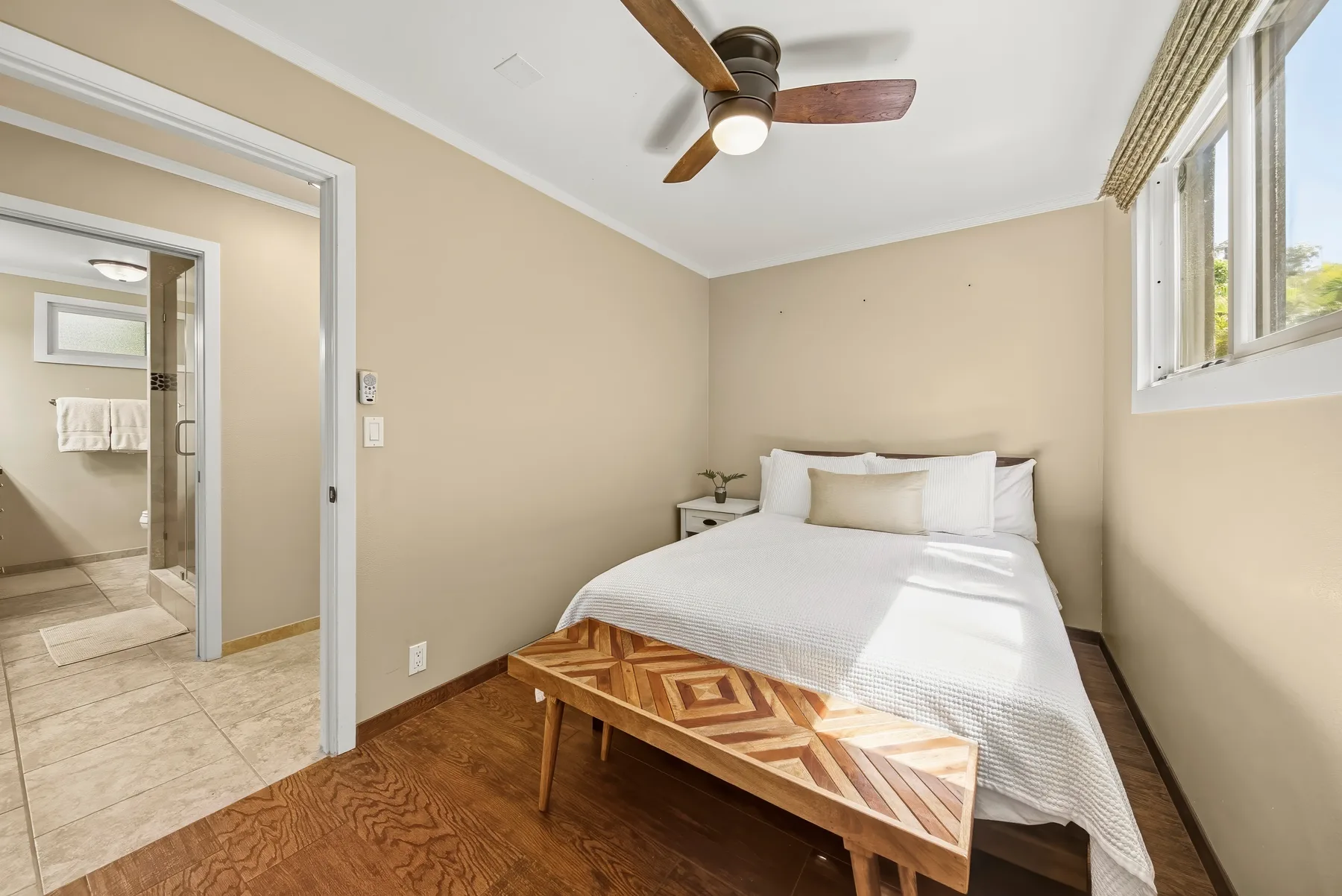 Un dormitorio con una cama bien tendida, un banco de madera y un ventilador de techo.