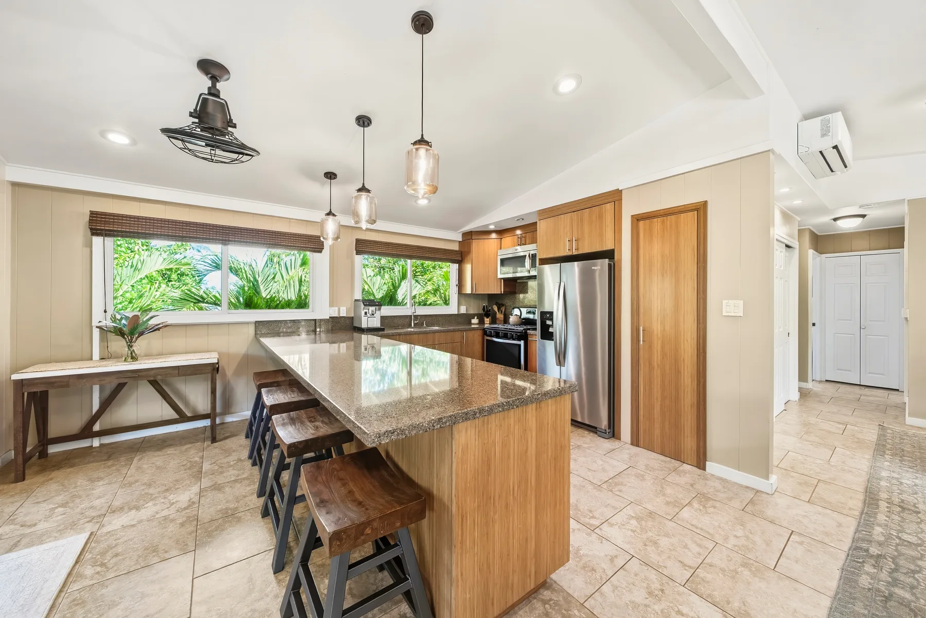 Una cocina luminosa con una isla central, asientos y ventanas con vistas a la vegetación.
