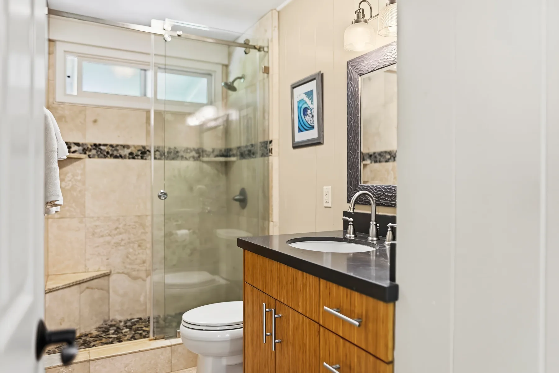 Un baño con ducha de vidrio, inodoro y mueble de lavabo con frente de madera.