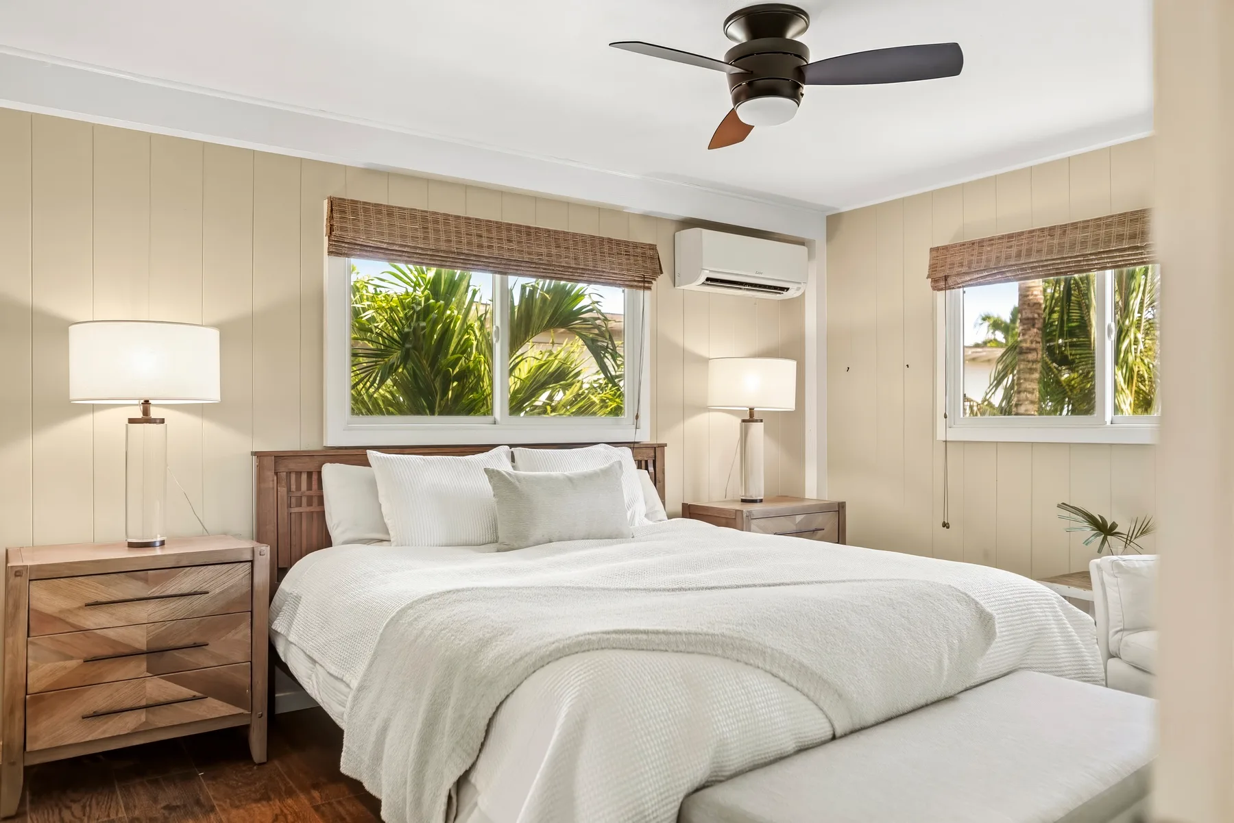 Un dormitorio con una cama bien tendida y ventanas con vistas a vegetación frondosa.