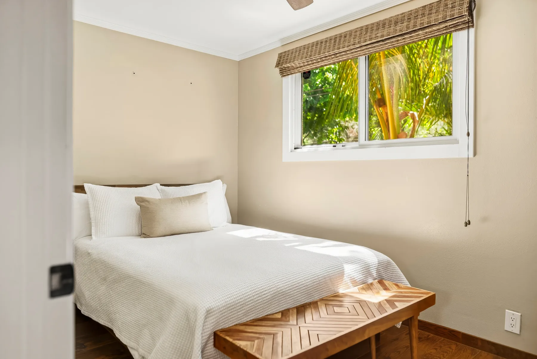Un dormitorio con una cama bien tendida junto a una ventana con vegetación.