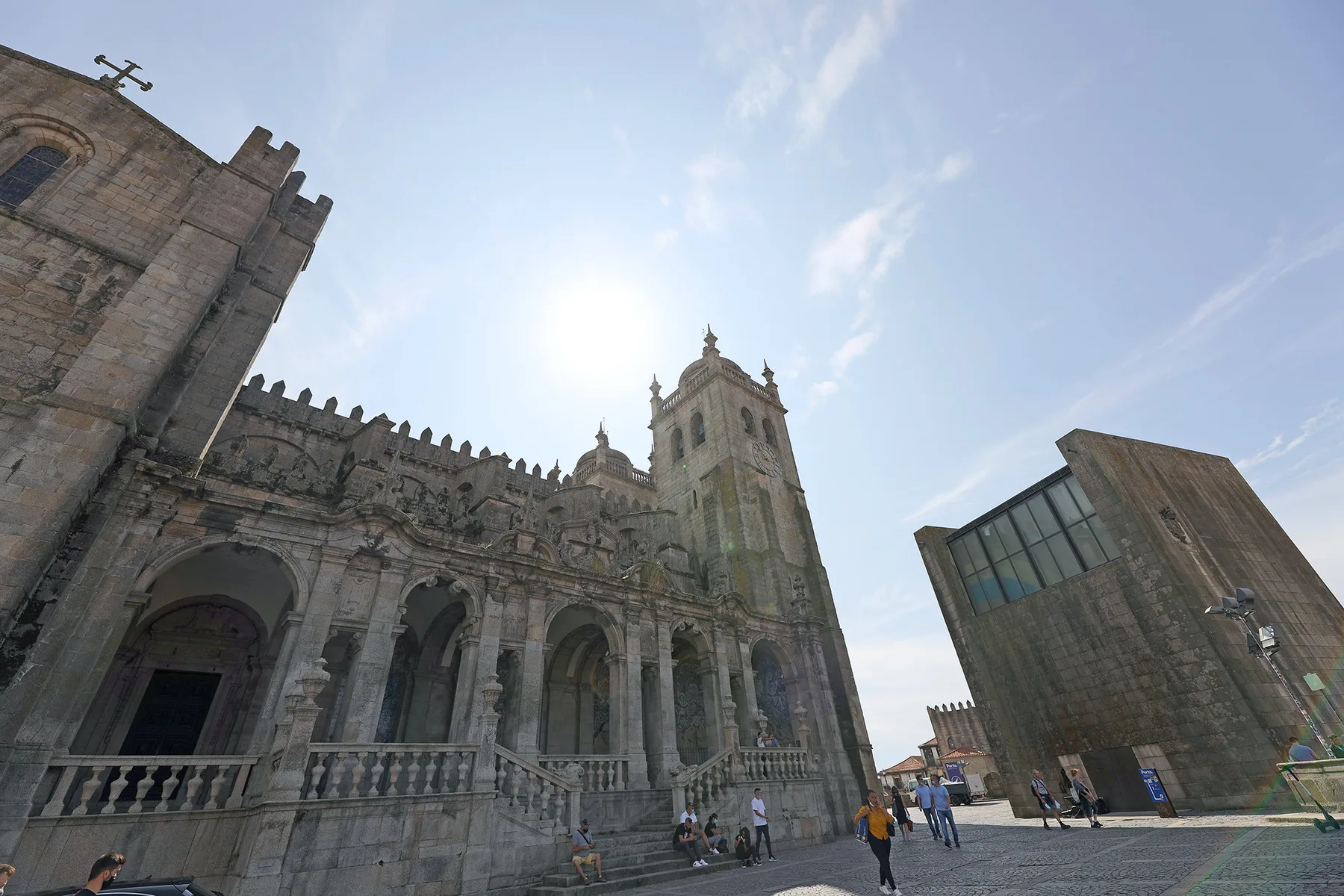 A historic stone church with a tall bell tower stands beside a modern glass-fronted building.