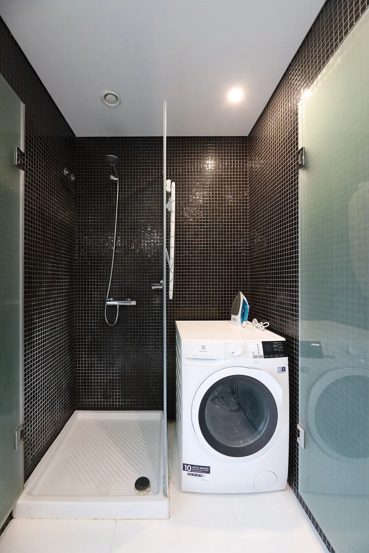 A tiled bathroom with a shower and a front-loading washing machine.