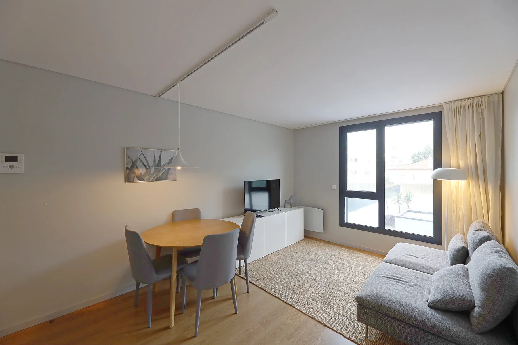 A living room with a dining table, seating, and a television beside a large window.