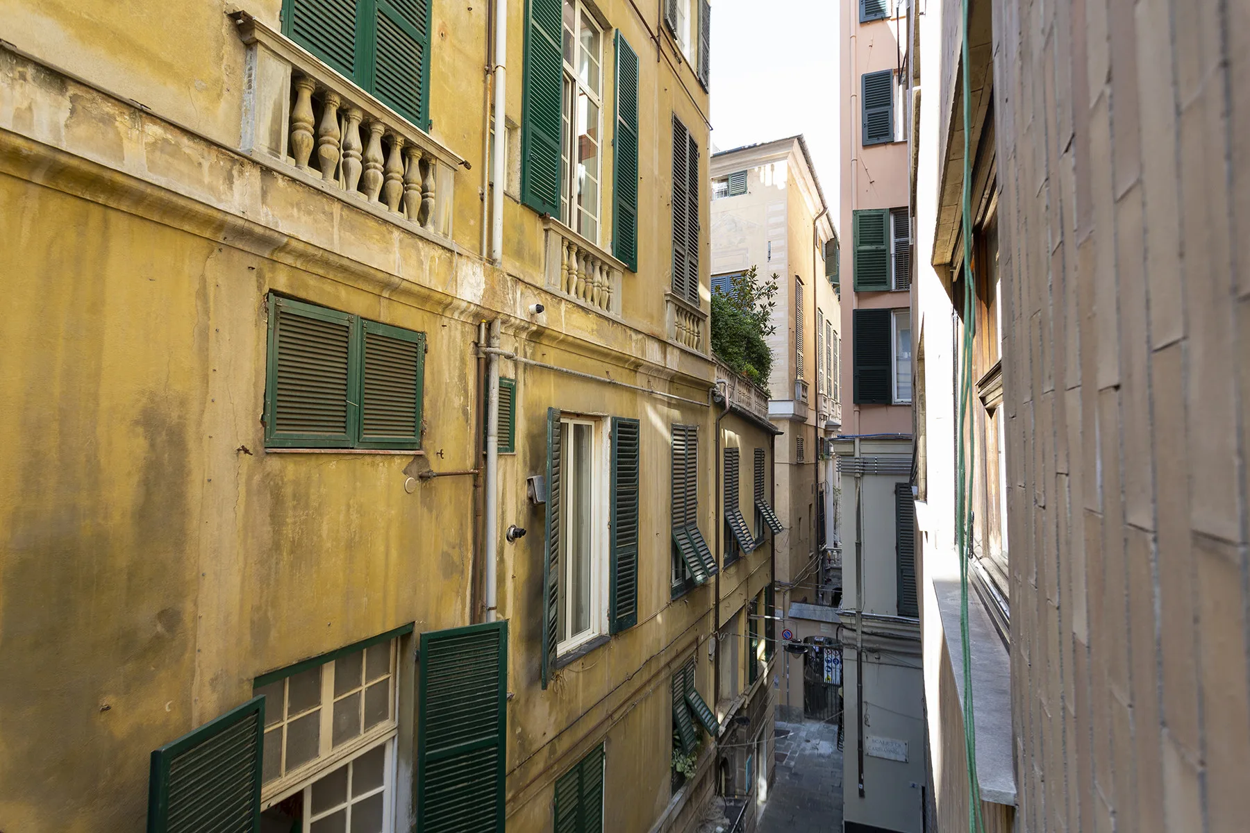A narrow alley runs between tall buildings with shuttered windows.