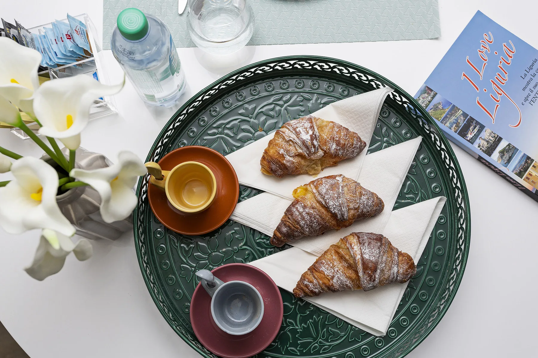 A tabletop displays pastries on a decorative tray beside cups and flowers.