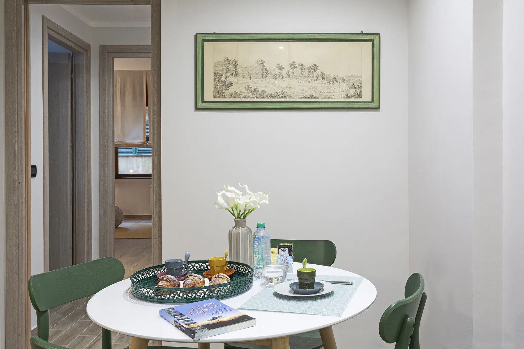 A dining area with a round table, green chairs, and framed artwork on the wall.