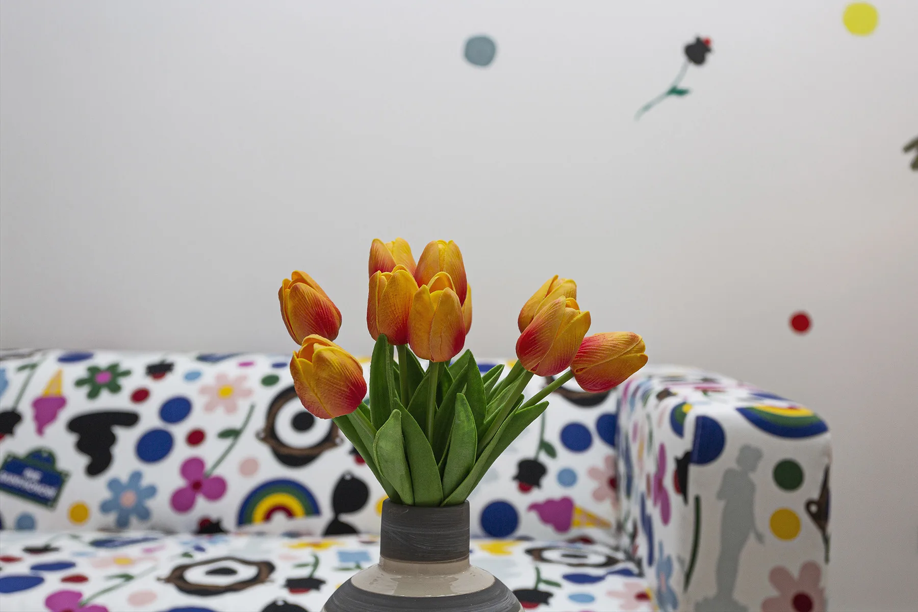 A colorful seating area has patterned upholstery and a vase of tulips.