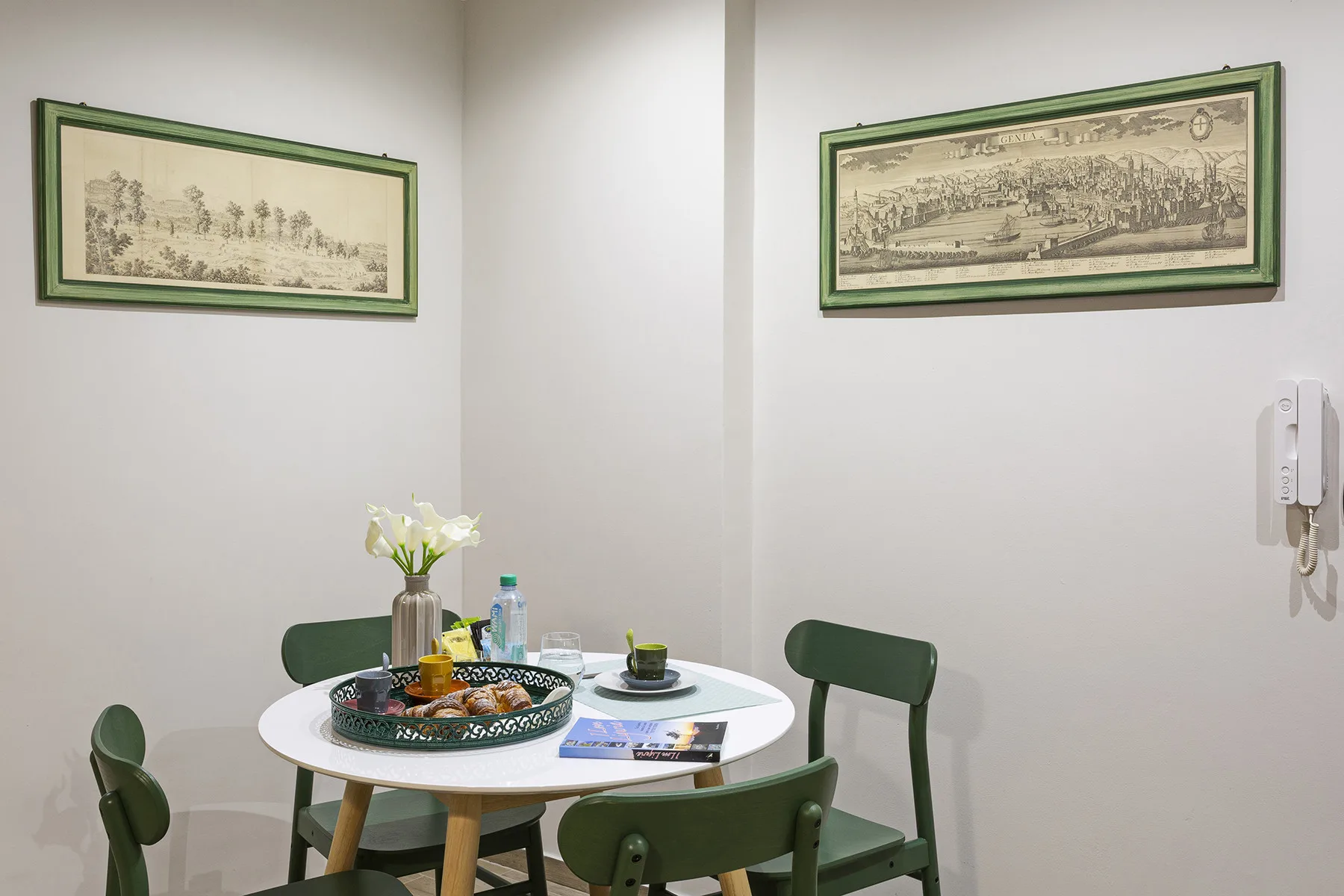 A small dining area with a round table, green seating, and framed wall art.