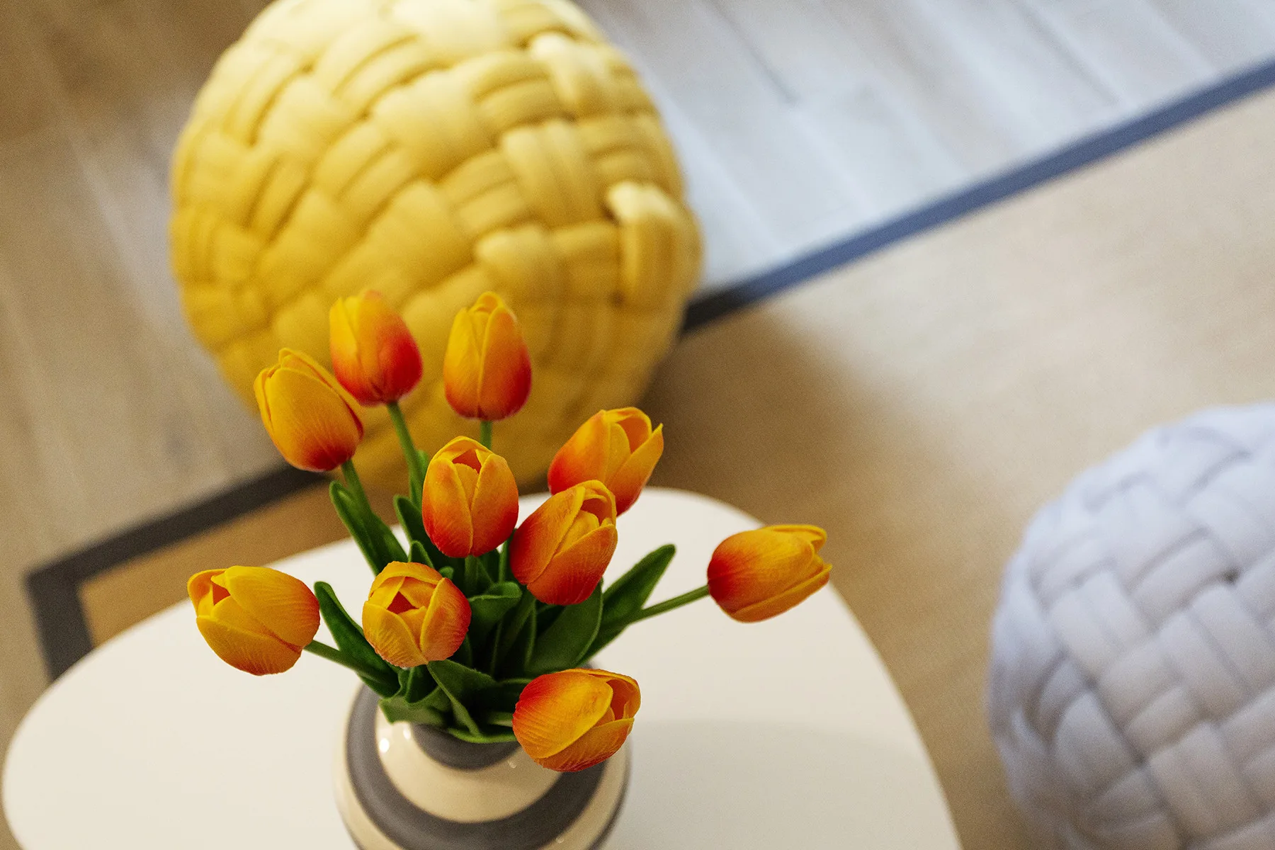 A vase of orange tulips sits on a round table beside woven decorative balls.