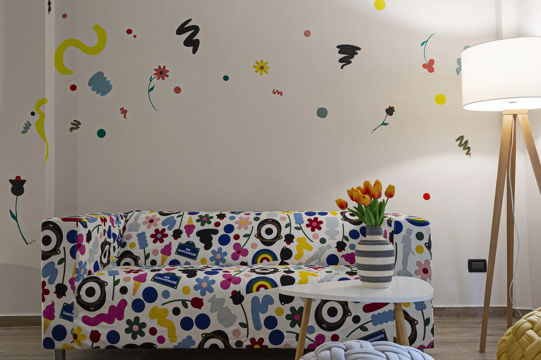 A colorful sitting area with patterned seating, a small table, and a floor lamp.