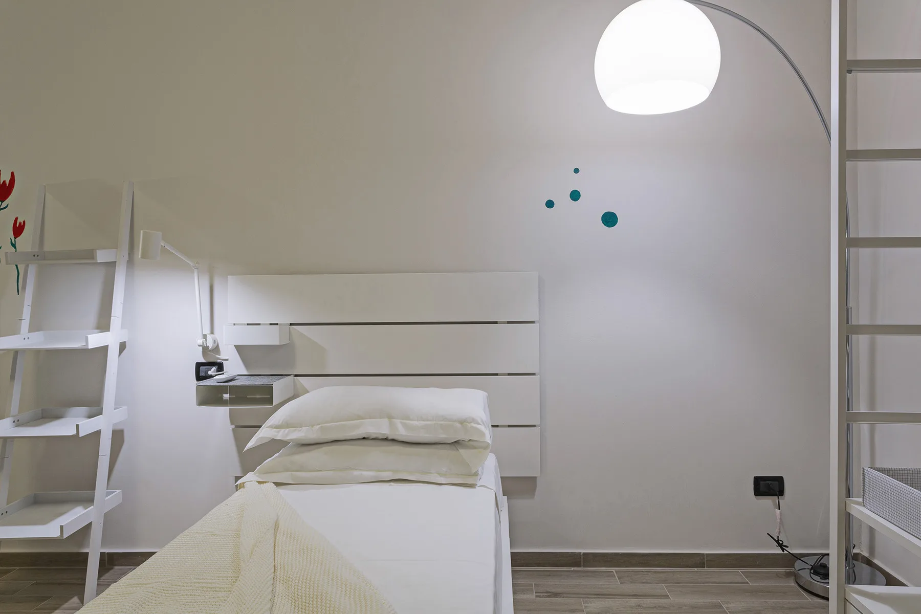 A bedroom with a single bed, white bedding, and a glowing pendant light.