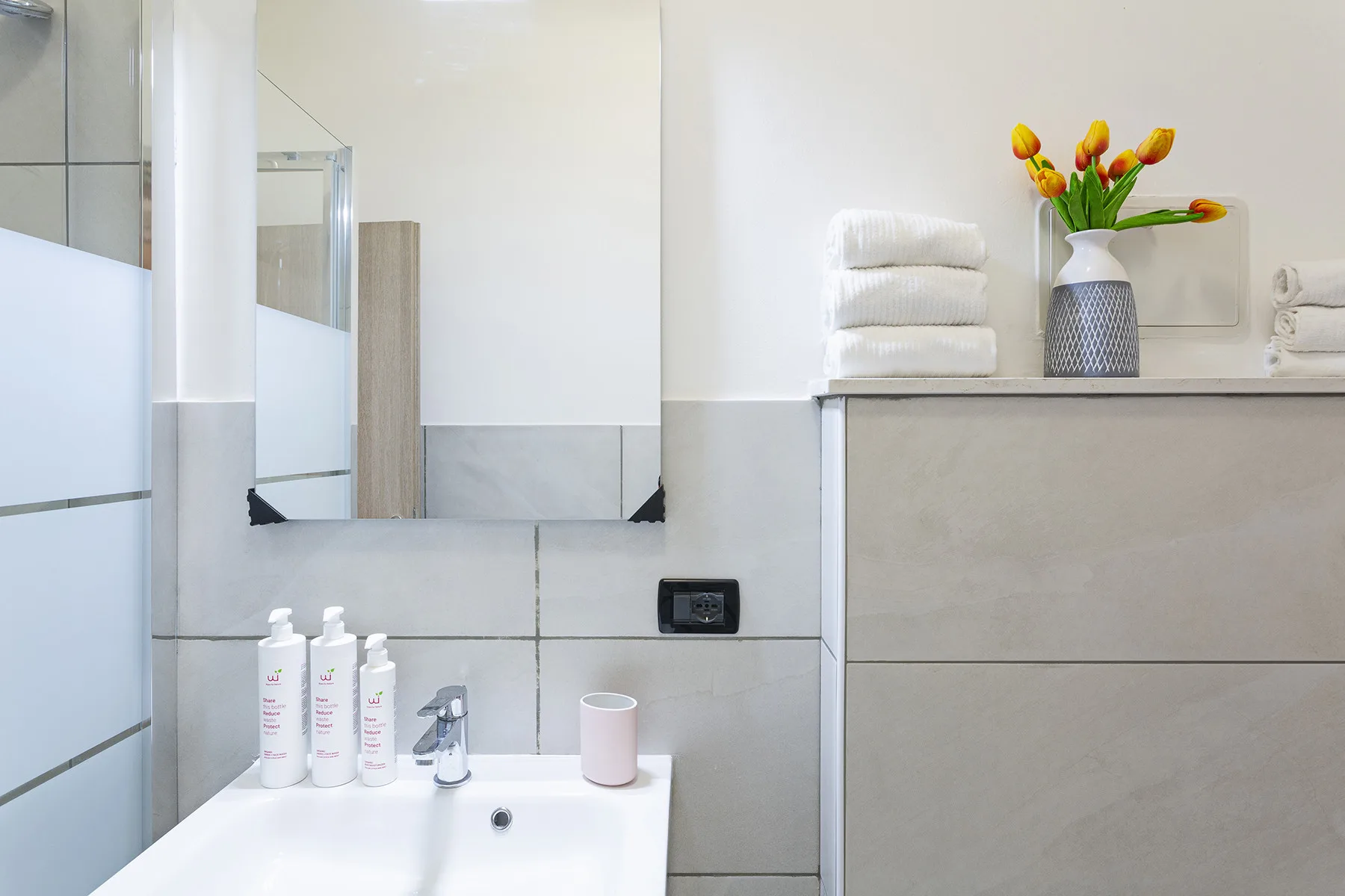 A bright bathroom with a sink, wall mirror, and folded towels.