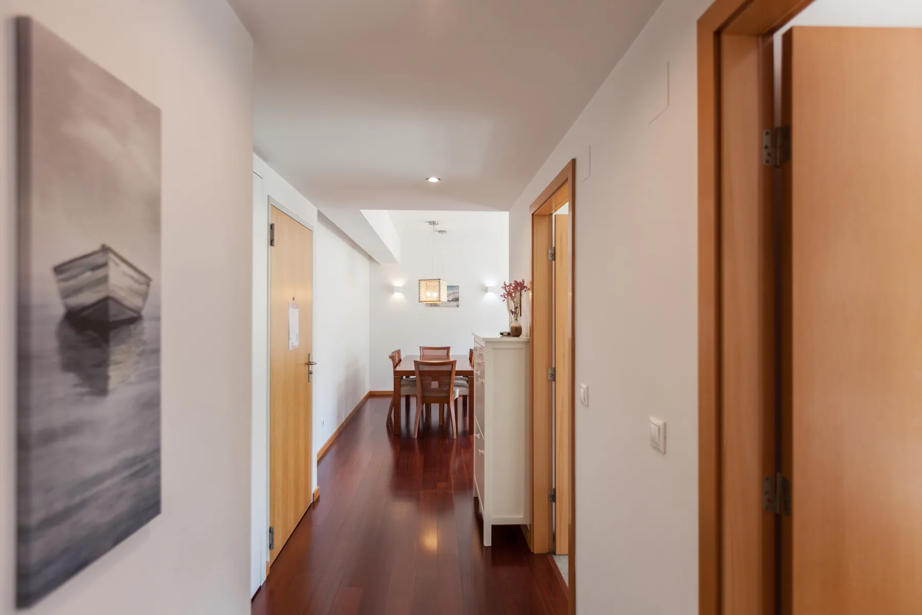 A bright apartment hallway leads to a dining area with a wooden table.