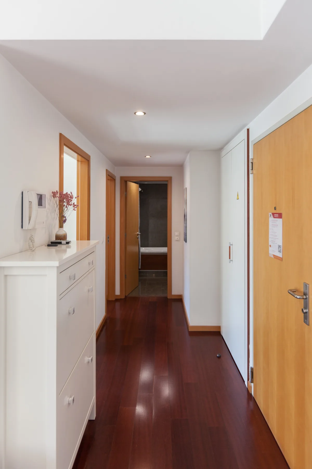 A bright hallway with polished wood flooring and white built-in storage.