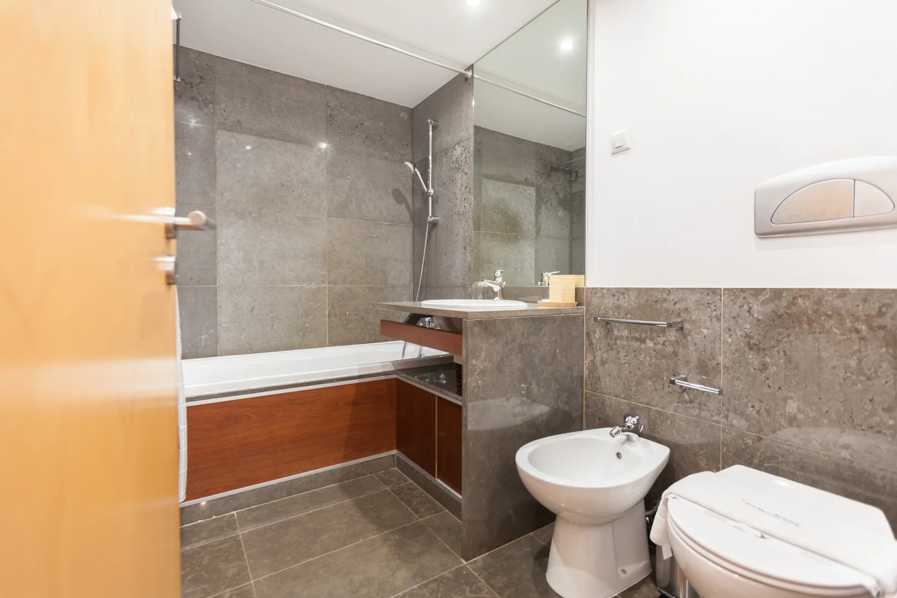 A bathroom with a bathtub, sink, and toilet beside a mirrored wall.