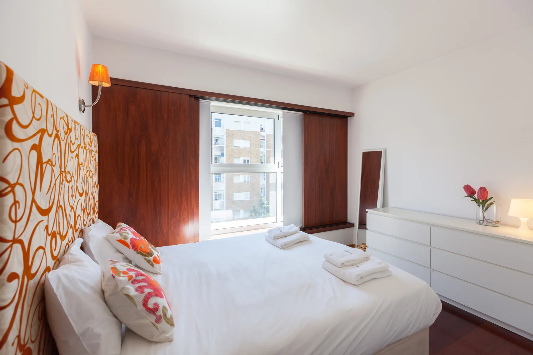 A bedroom with a bed, patterned wall, window, and dresser.