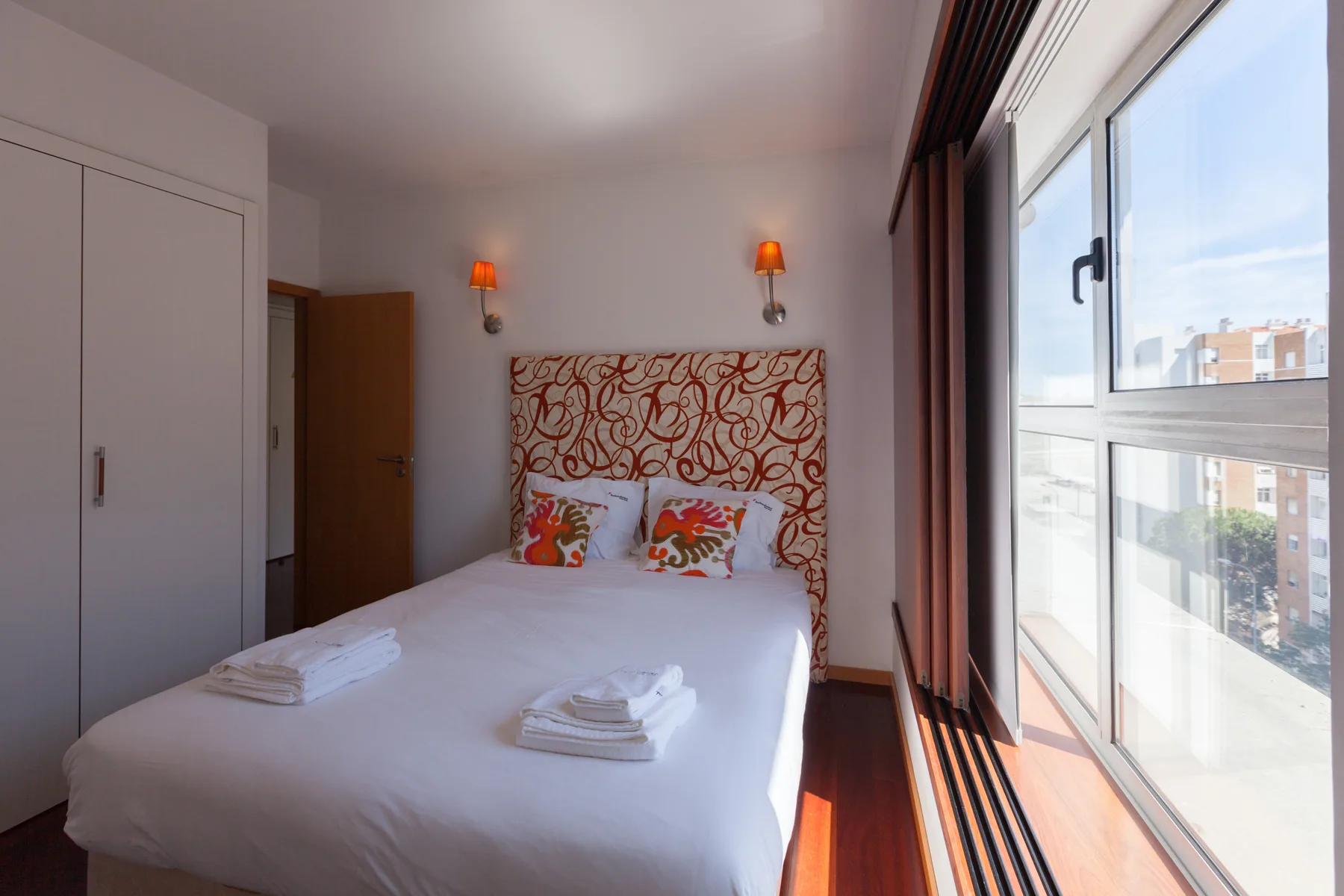 A bright bedroom with a bed beside a large window.