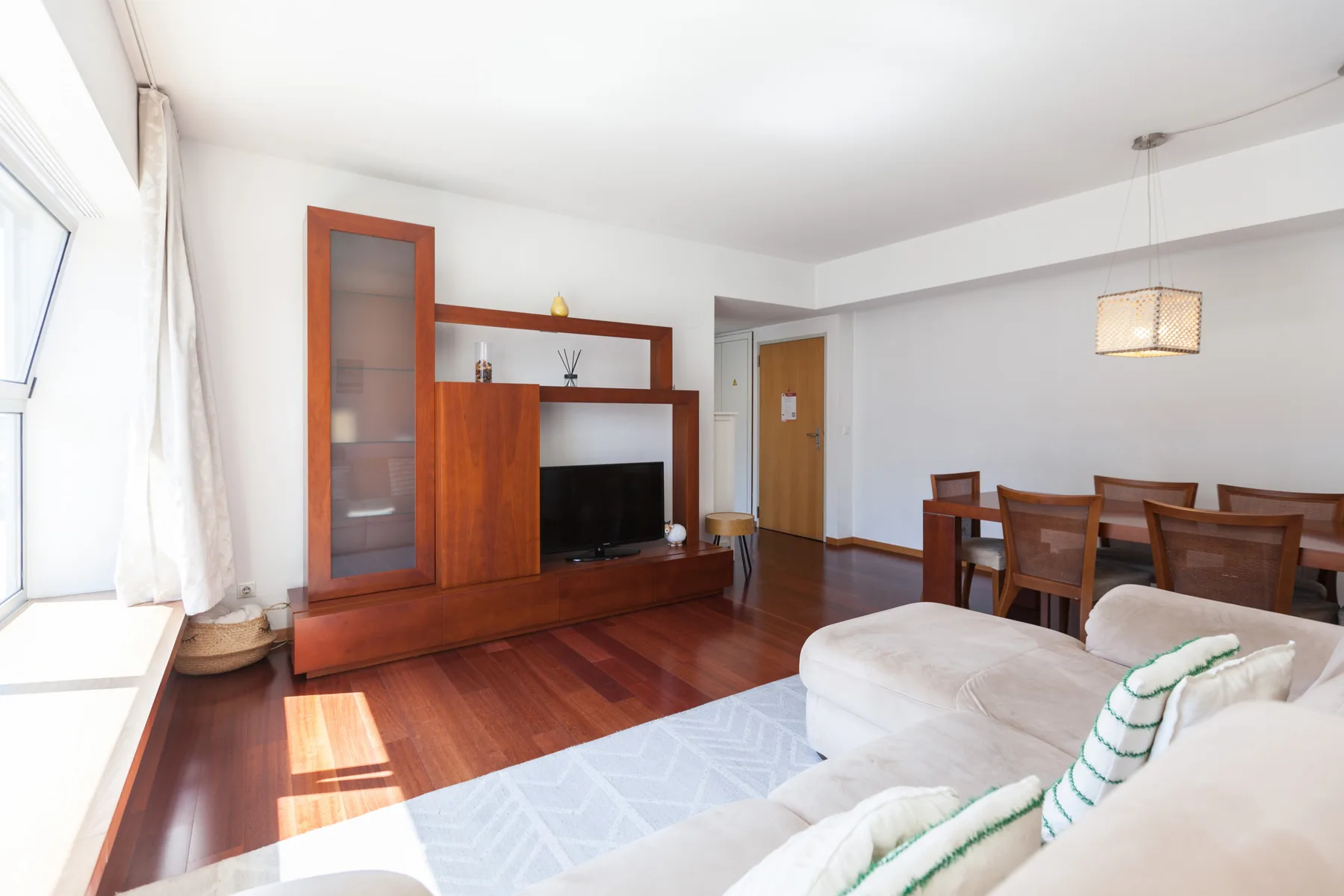 A bright living and dining area with wooden flooring and a television.