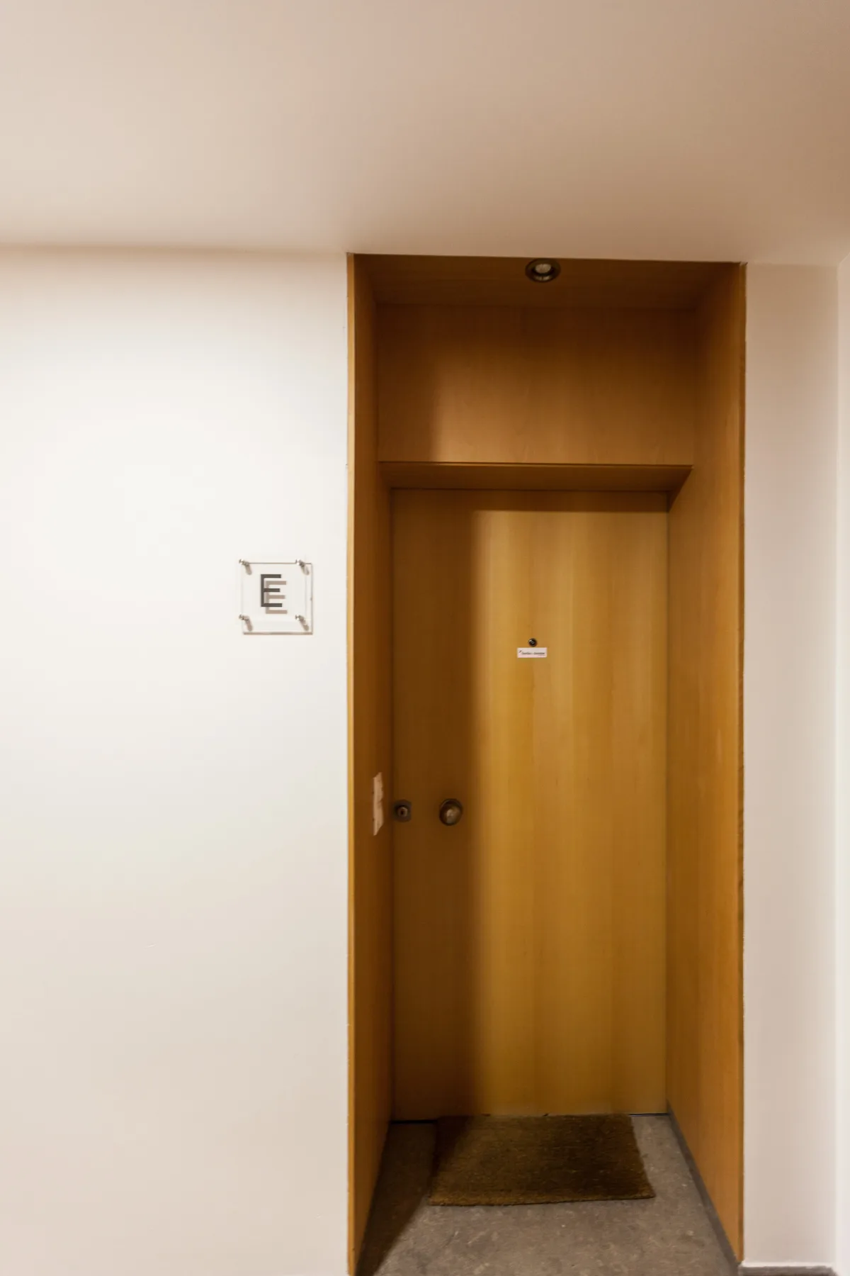 A wooden entry door sits within a recessed hallway.