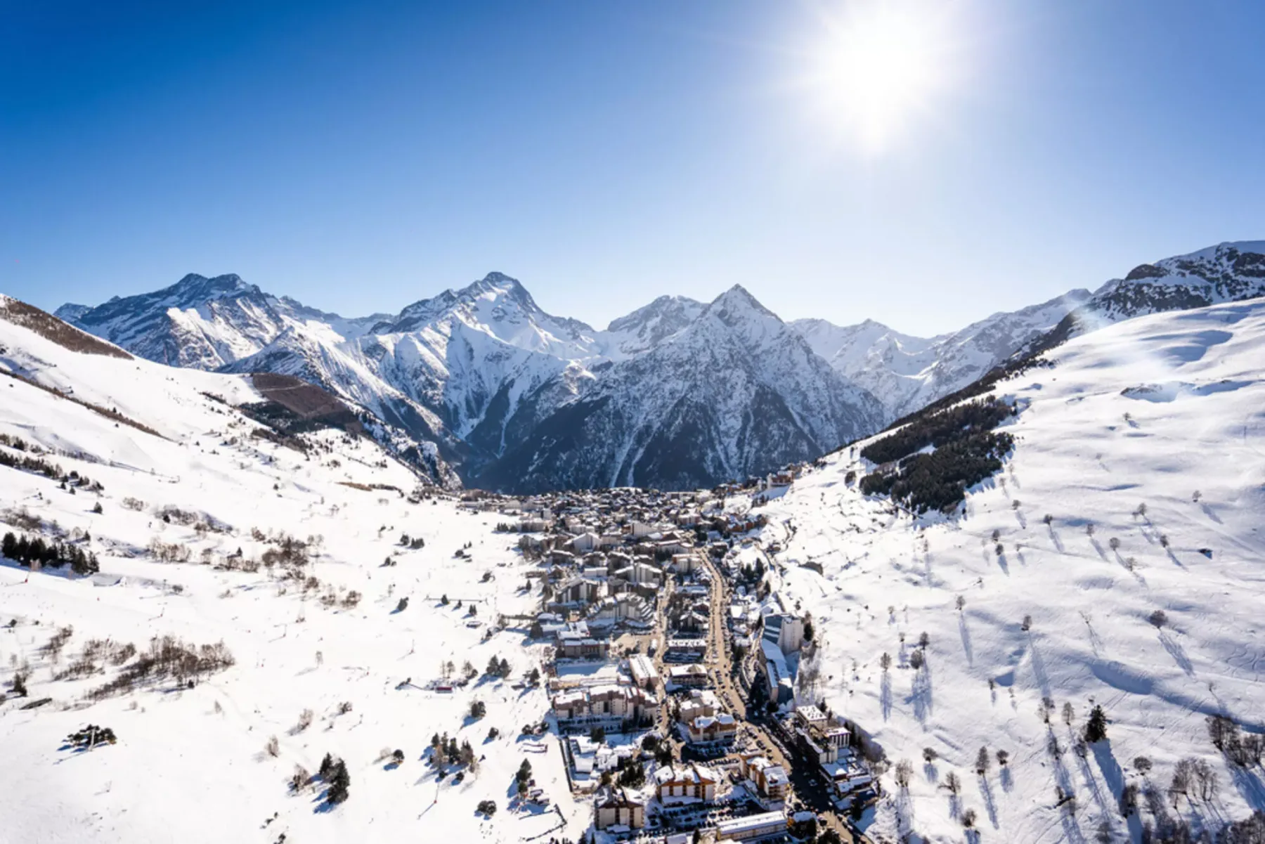 Un pueblo cubierto de nieve se encuentra en un amplio valle alpino bajo un cielo soleado.