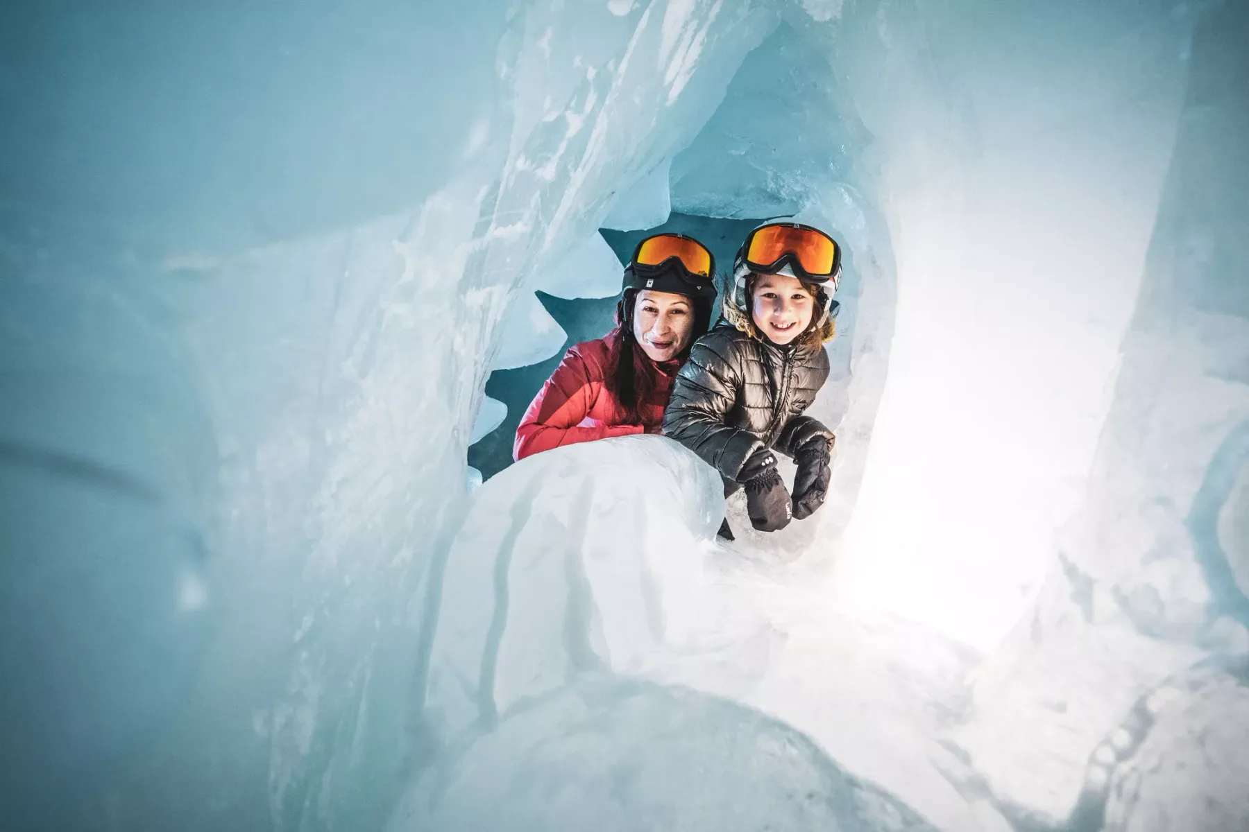 Dos personas con ropa de invierno posan dentro de una cueva de hielo azul.