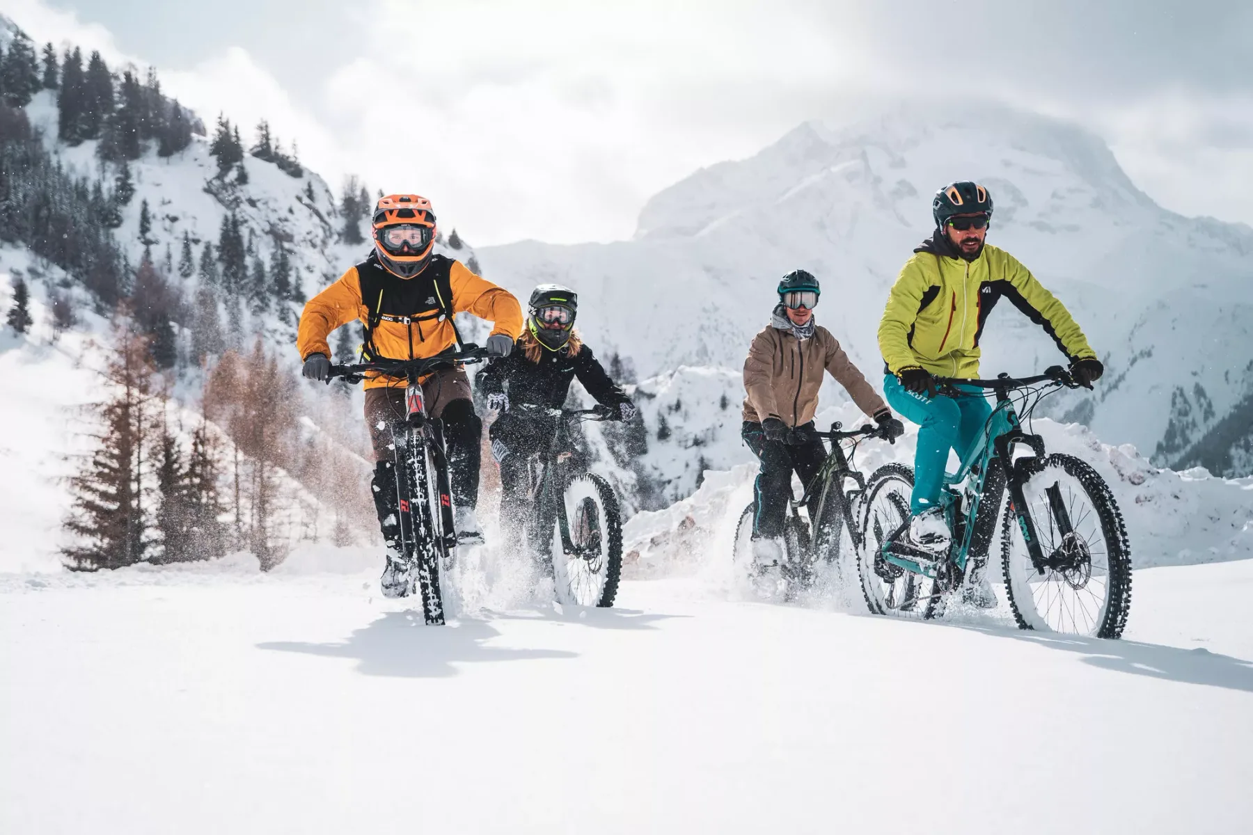 Ciclistas recorren un sendero nevado de montaña en bicicletas de ruedas anchas.